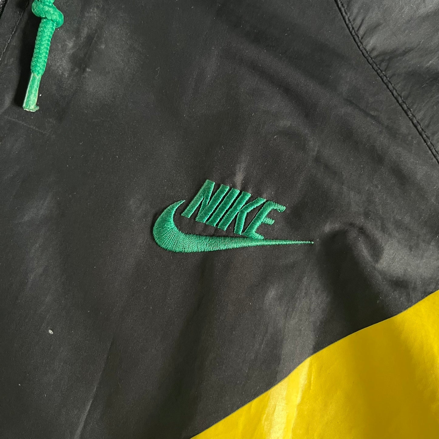 Nike Jamaica Olympics 2008 Split Windbreaker designed by Jarrett Reynolds. Features a black base with a yellow cross on the front inspired by the Jamaican flag. Green bottom hem and details. Dual side zippers allow the jacket to split in half and be combined with other pieces from the collection, with a small Jamaica flag detail inside the pocket.
