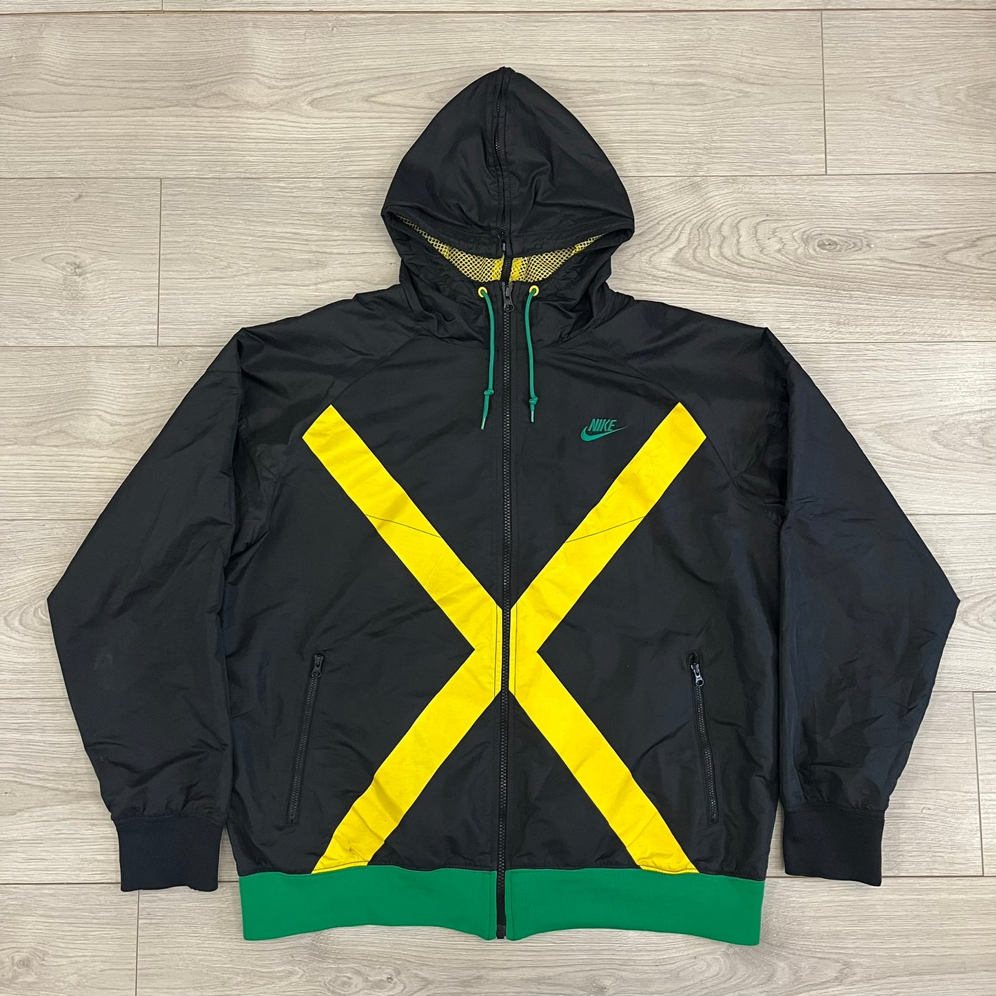 Nike Jamaica Olympics 2008 Split Windbreaker designed by Jarrett Reynolds. Features a black base with a yellow cross on the front inspired by the Jamaican flag. Green bottom hem and details. Dual side zippers allow the jacket to split in half and be combined with other pieces from the collection, with a small Jamaica flags detail inside the pocket.