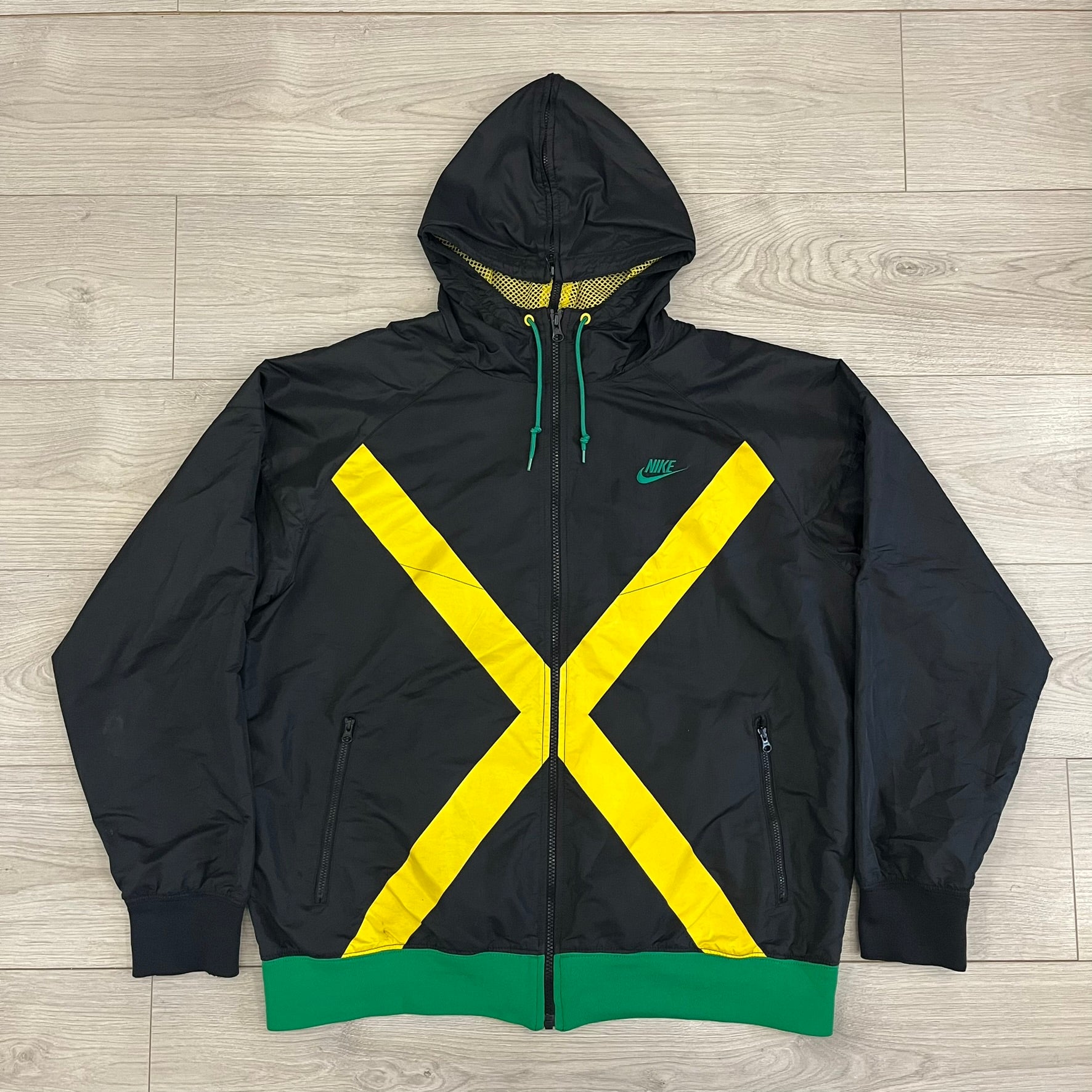 Nike Jamaica Olympics 2008 Split Windbreaker designed by Jarrett Reynolds. Features a black base with a yellow cross on the front inspired by the Jamaican flag. Green bottom hem and details. Dual side zippers allow the jacket to split in half and be combined with other pieces from the collection, with a small Jamaica flags detail inside the pocket.