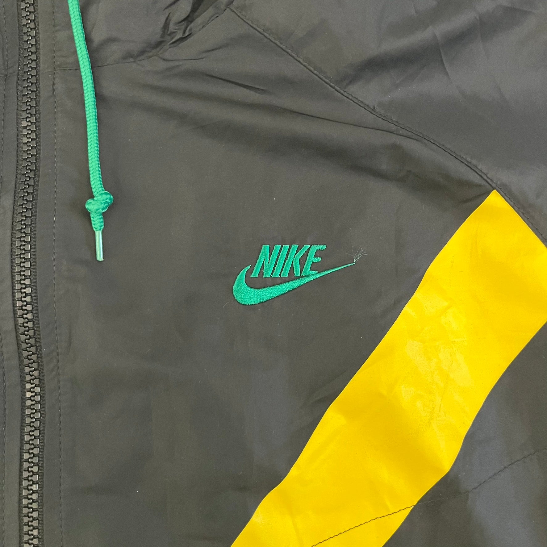 Nike Jamaica Olympics 2008 Split Windbreaker designed by Jarrett Reynolds. Features a black base with a yellow cross on the front inspired by the Jamaican flag. Green bottom hem and details. Dual side zippers allow the jacket to split in half and be combined with other pieces from the collection, with a small Jamaica flags detail inside the pocket.