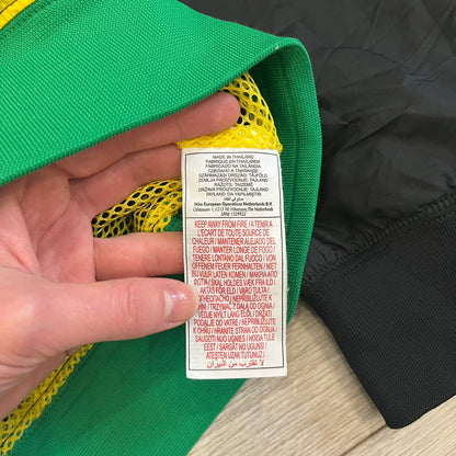 Nike Jamaica Olympics 2008 Split Windbreaker designed by Jarrett Reynolds. Features a black base with a yellow cross on the front inspired by the Jamaican flag. Green bottom hem and details. Dual side zippers allow the jacket to split in half and be combined with other pieces from the collection, with a small Jamaica flags detail inside the pocket.