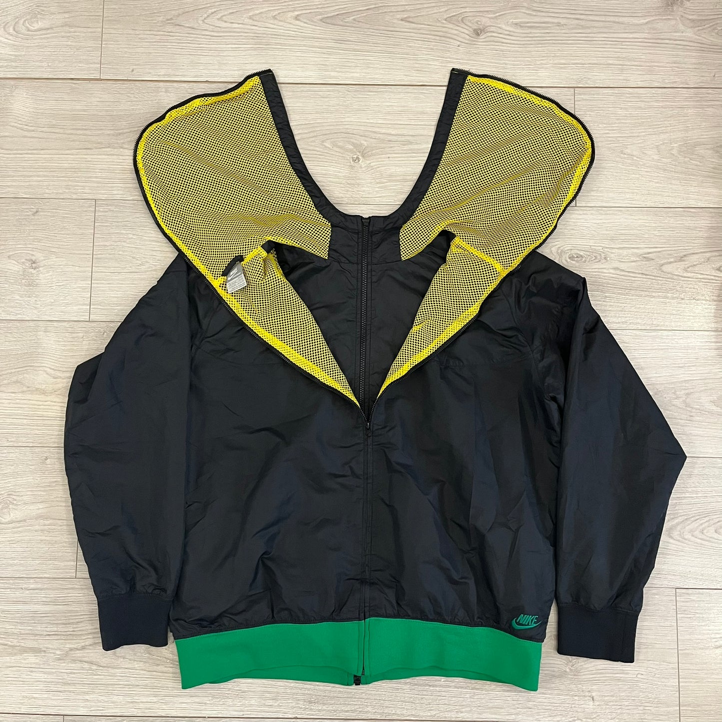 Nike Jamaica Olympics 2008 Split Windbreaker designed by Jarrett Reynolds. Features a black base with a yellow cross on the front inspired by the Jamaican flag. Green bottom hem and details. Dual side zippers allow the jacket to split in half and be combined with other pieces from the collection, with a small Jamaica flags detail inside the pocket.