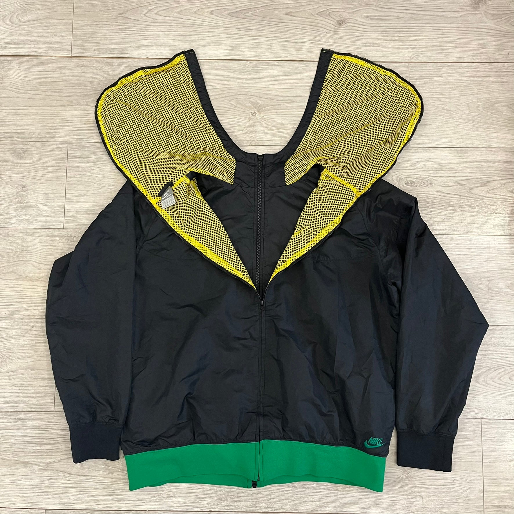 Nike Jamaica Olympics 2008 Split Windbreaker designed by Jarrett Reynolds. Features a black base with a yellow cross on the front inspired by the Jamaican flag. Green bottom hem and details. Dual side zippers allow the jacket to split in half and be combined with other pieces from the collection, with a small Jamaica flags detail inside the pocket.