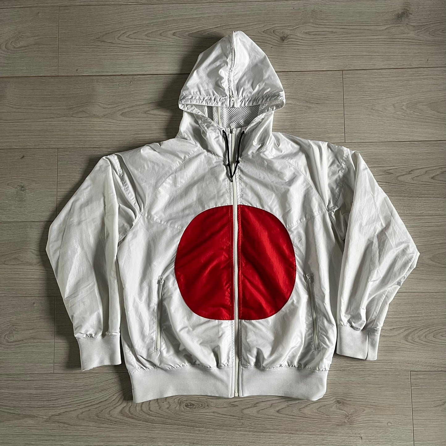 Nike Japan Olympics Split Windbreaker from 2008, created by designer Jarrett Reynolds. Crafted in white with a large red circle representing Japan’s flag, this innovative jacket can be zipped apart on both sides and merged with other compatible models. Hidden inside, a small Japan flag accent completes the concept.