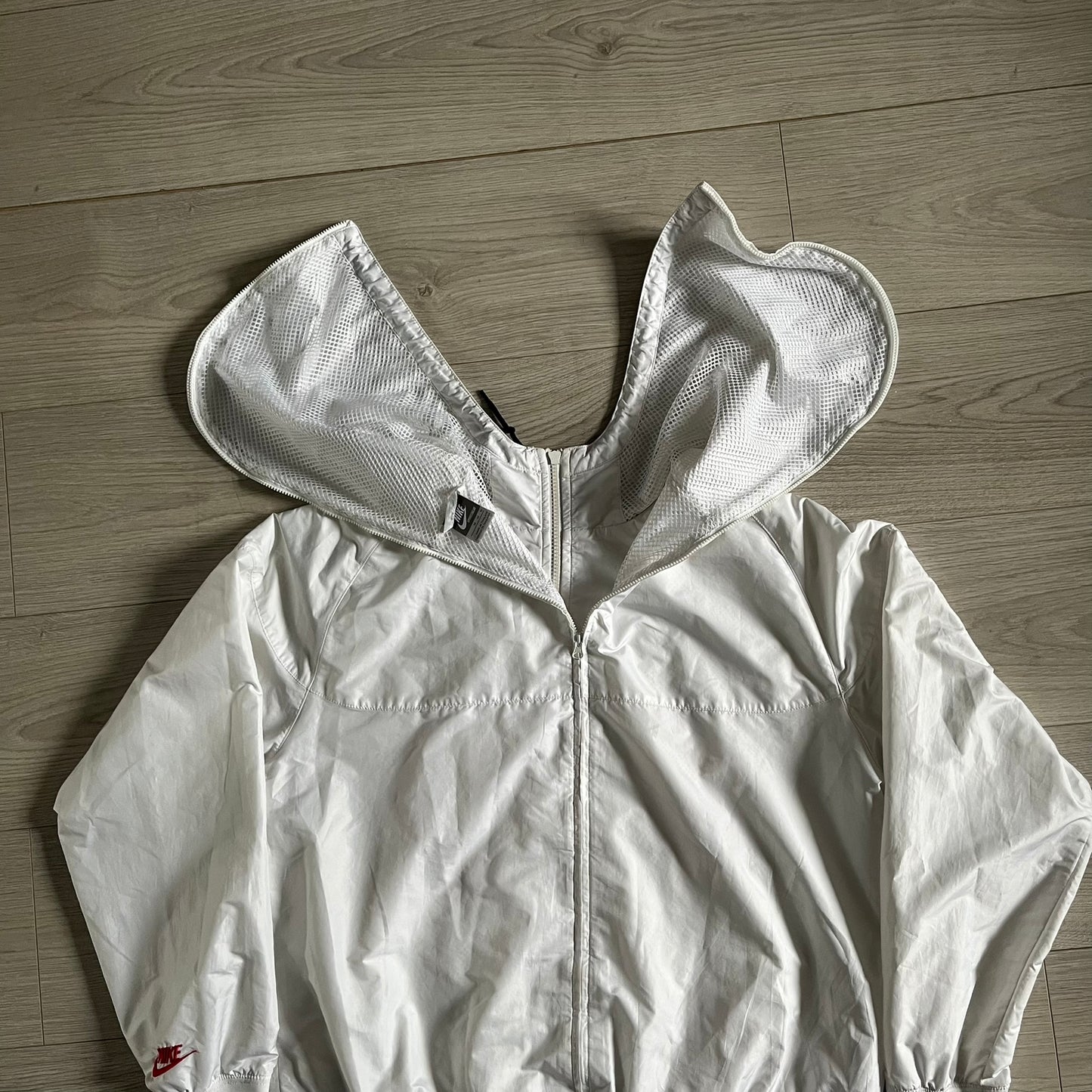 Nike Japan Olympics Split Windbreaker from 2008, created by designer Jarrett Reynolds. Crafted in white with a large red circle representing Japan’s flag, this innovative jacket can be zipped apart on both sides and merged with other compatible models. Hidden inside, a small Japan flag accent completes the concept.