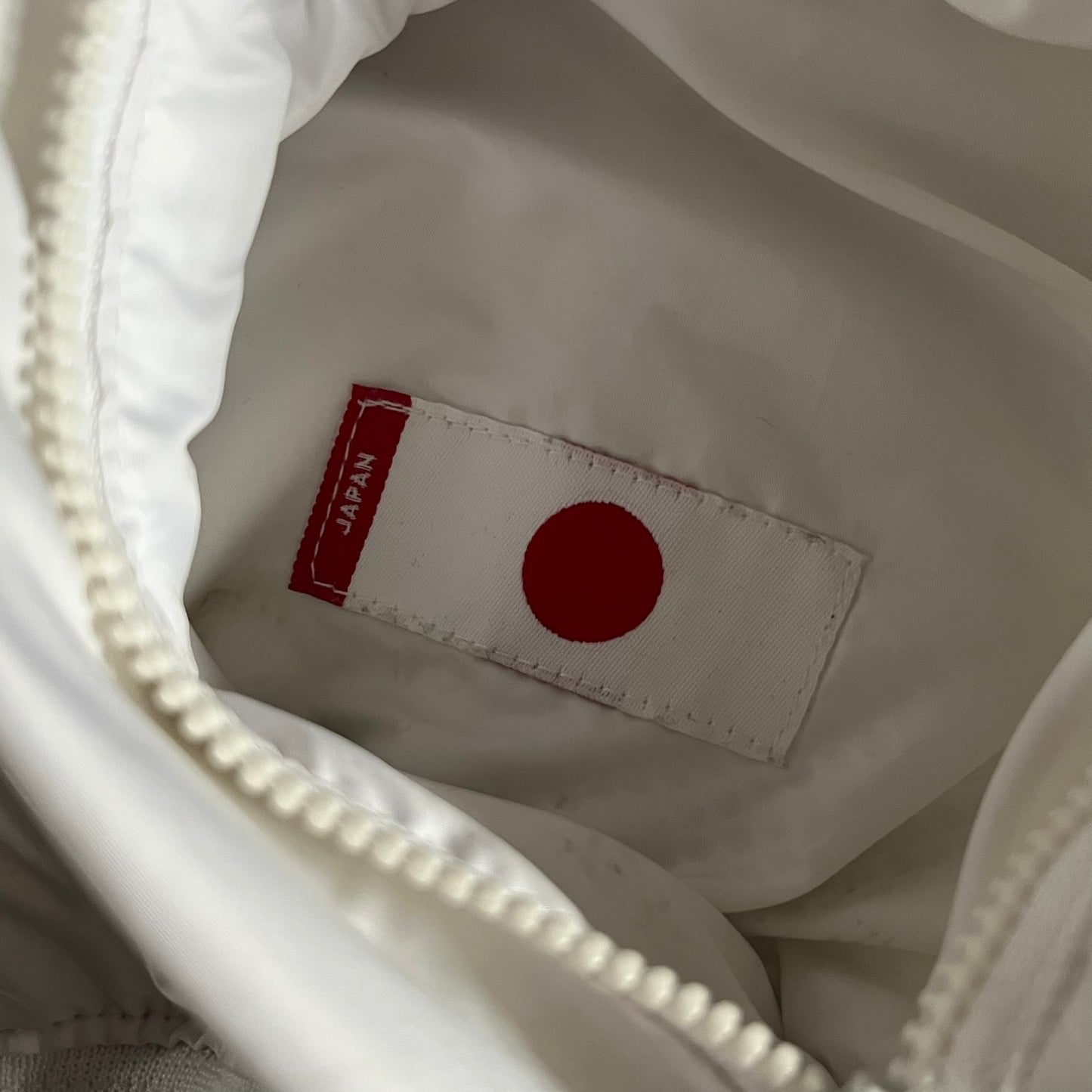 Nike Japan Olympics Split Windbreaker from 2008, created by designer Jarrett Reynolds. Crafted in white with a large red circle representing Japan’s flag, this innovative jacket can be zipped apart on both sides and merged with other compatible models. Hidden inside, a small Japan flag accent completes the concept.