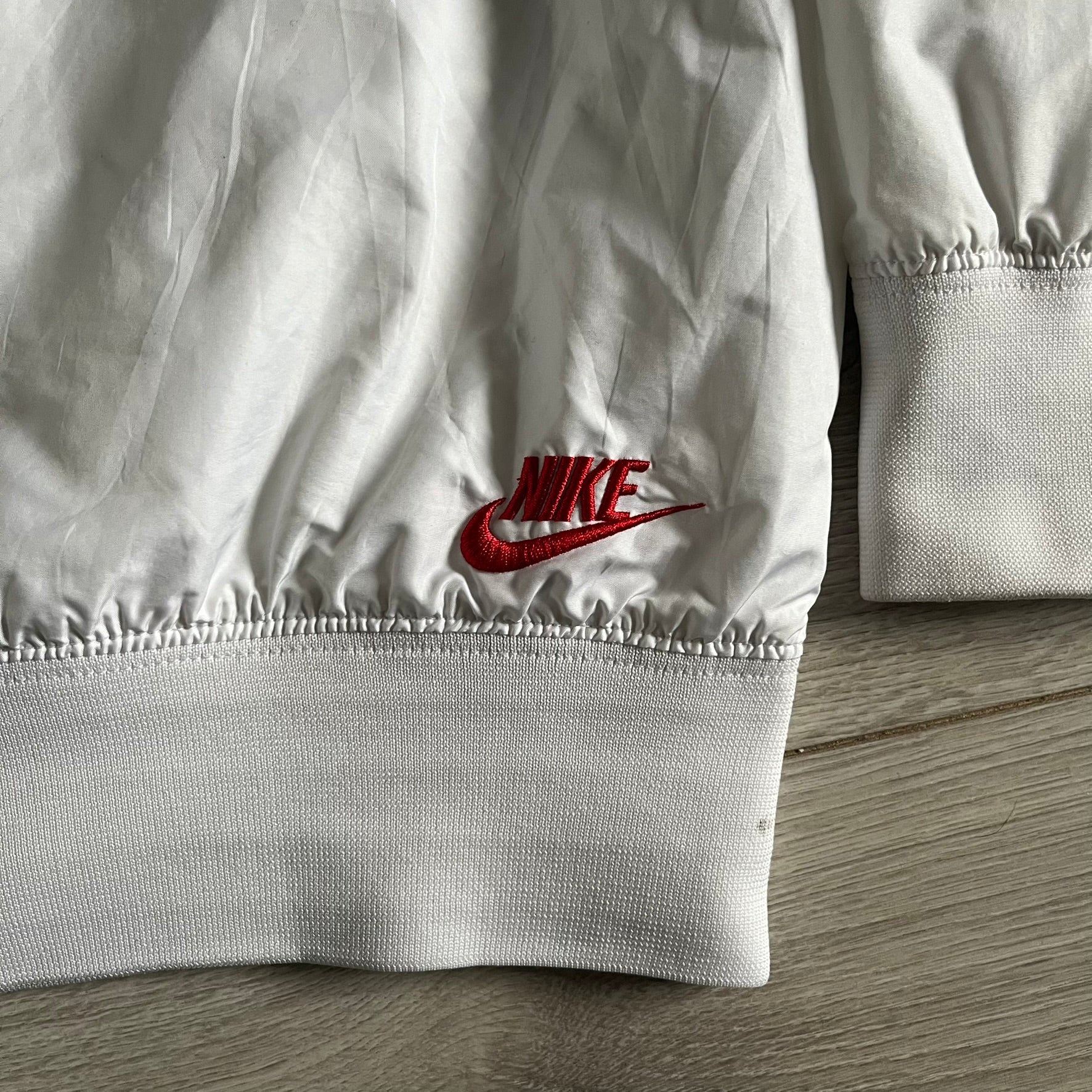 Nike Japan Olympics Split Windbreaker from 2008, created by designer Jarrett Reynolds. Crafted in white with a large red circle representing Japan’s flag, this innovative jacket can be zipped apart on both sides and merged with other compatible models. Hidden inside, a small Japan flag accent completes the concept.