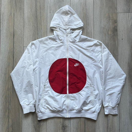 Nike Japan Olympics Split Windbreaker from 2008, created by designer Jarrett Reynolds. Crafted in white with a large red circle representing Japan’s flag, this innovative jacket can be zipped apart on both sides and merged with other compatible models. Hidden inside, a small Japan flags accent completes the concept.