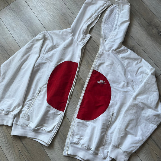 Nike Japan Olympics Split Windbreaker from 2008, created by designer Jarrett Reynolds. Crafted in white with a large red circle representing Japan’s flag, this innovative jacket can be zipped apart on both sides and merged with other compatible models. Hidden inside, a small Japan flags accent completes the concept.