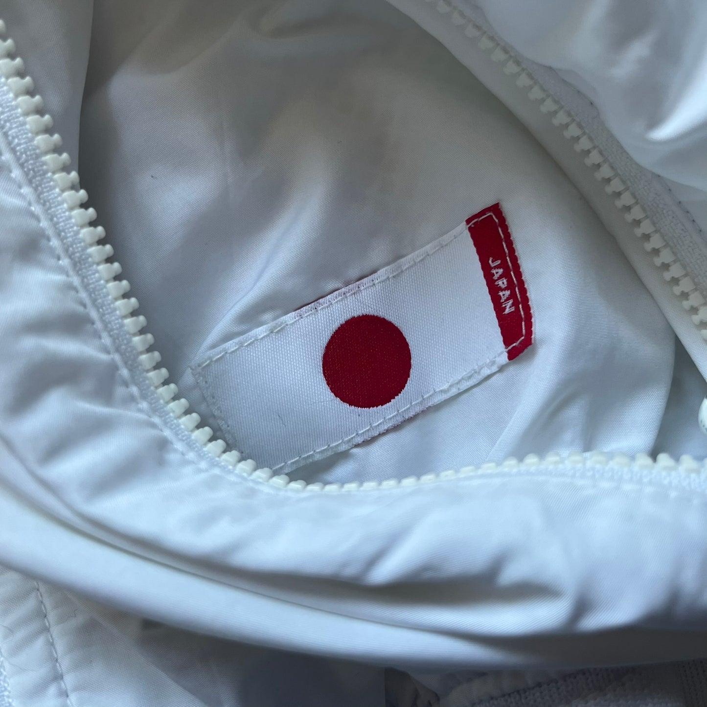 Nike Japan Olympics Split Windbreaker from 2008, created by designer Jarrett Reynolds. Crafted in white with a large red circle representing Japan’s flag, this innovative jacket can be zipped apart on both sides and merged with other compatible models. Hidden inside, a small Japan flags accent completes the concept.