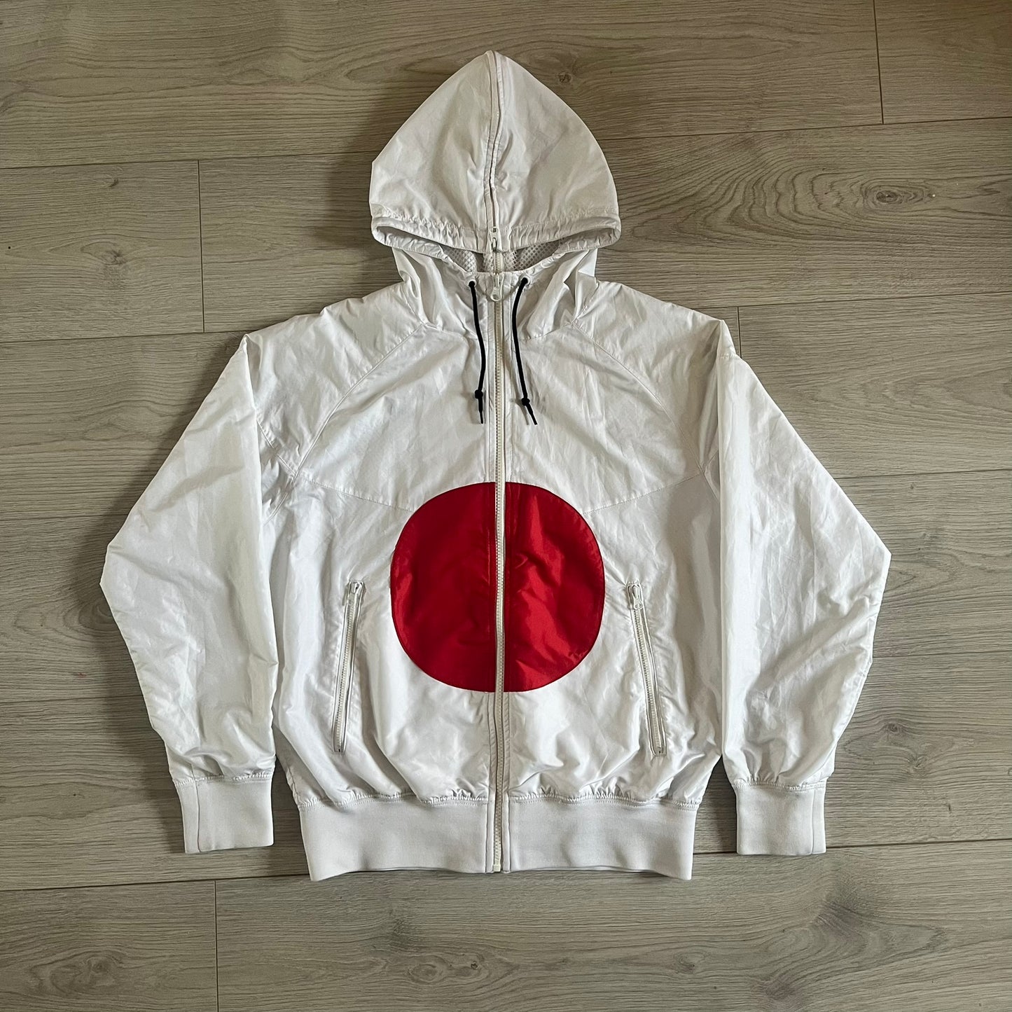 Nike Japan Olympics Split Windbreaker from 2008, created by designer Jarrett Reynolds. Crafted in white with a large red circle representing Japan’s flag, this innovative jacket can be zipped apart on both sides and merged with other compatible models. Hidden inside, a small Japan flags accent completes the concept.
