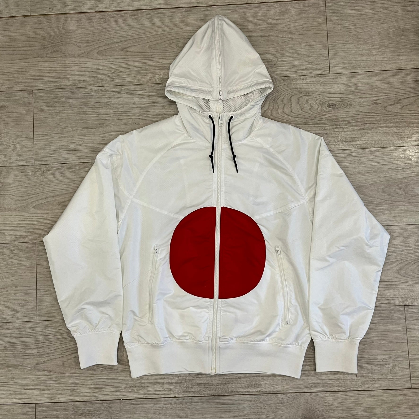 Nike Japan Olympics Split Windbreaker from 2008, created by designer Jarrett Reynolds. Crafted in white with a large red circle representing Japan’s flag, this innovative jacket can be zipped apart on both sides and merged with other compatible models. Hidden inside, a small Japan flags accent completes the concept.