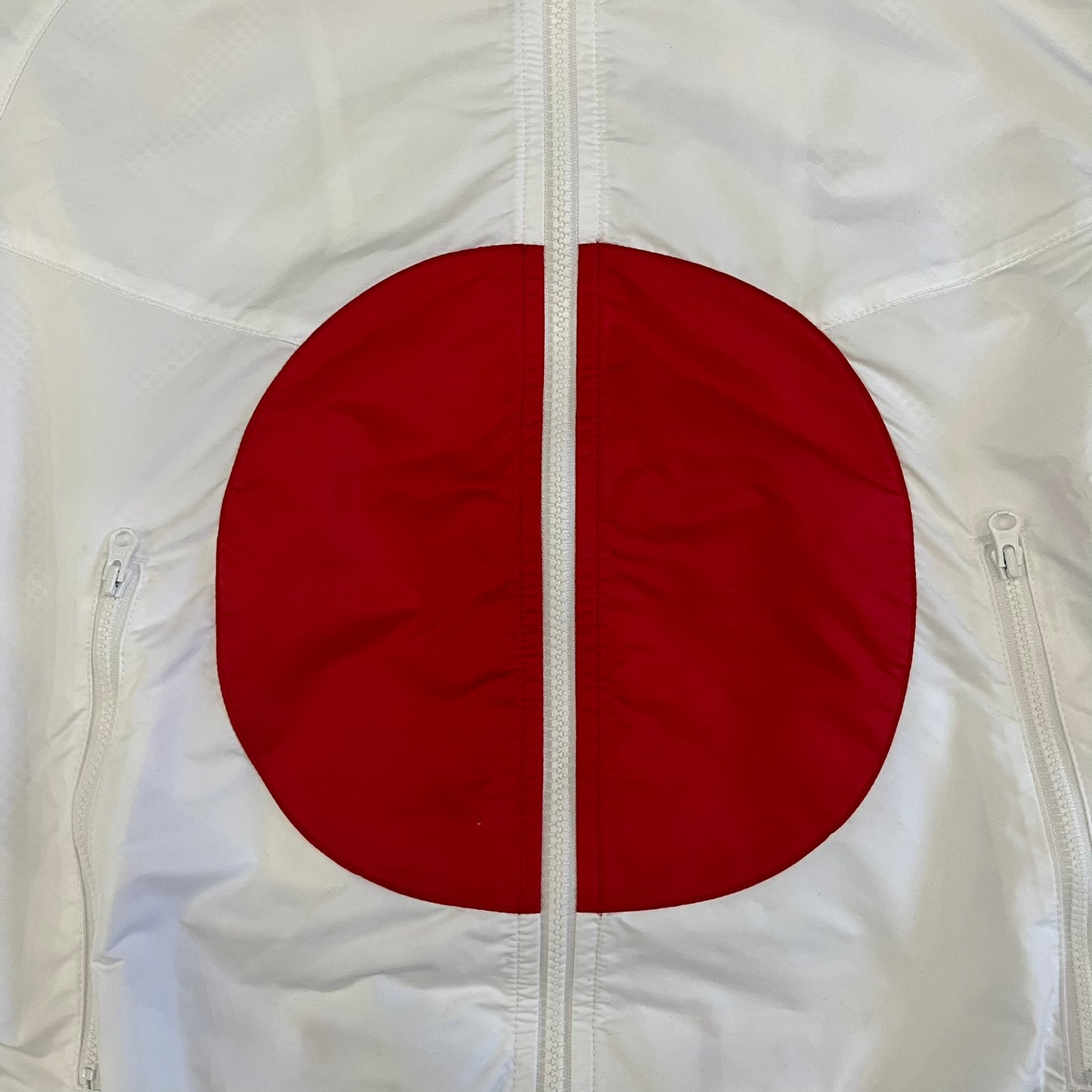 Nike Japan Olympics Split Windbreaker from 2008, created by designer Jarrett Reynolds. Crafted in white with a large red circle representing Japan’s flag, this innovative jacket can be zipped apart on both sides and merged with other compatible models. Hidden inside, a small Japan flags accent completes the concept.