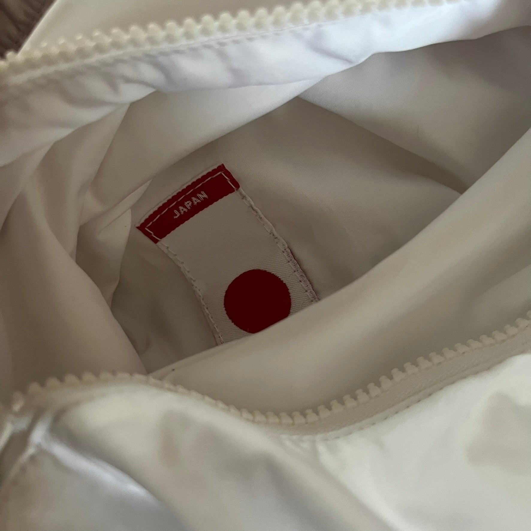 Nike Japan Olympics Split Windbreaker from 2008, created by designer Jarrett Reynolds. Crafted in white with a large red circle representing Japan’s flag, this innovative jacket can be zipped apart on both sides and merged with other compatible models. Hidden inside, a small Japan flags accent completes the concept.