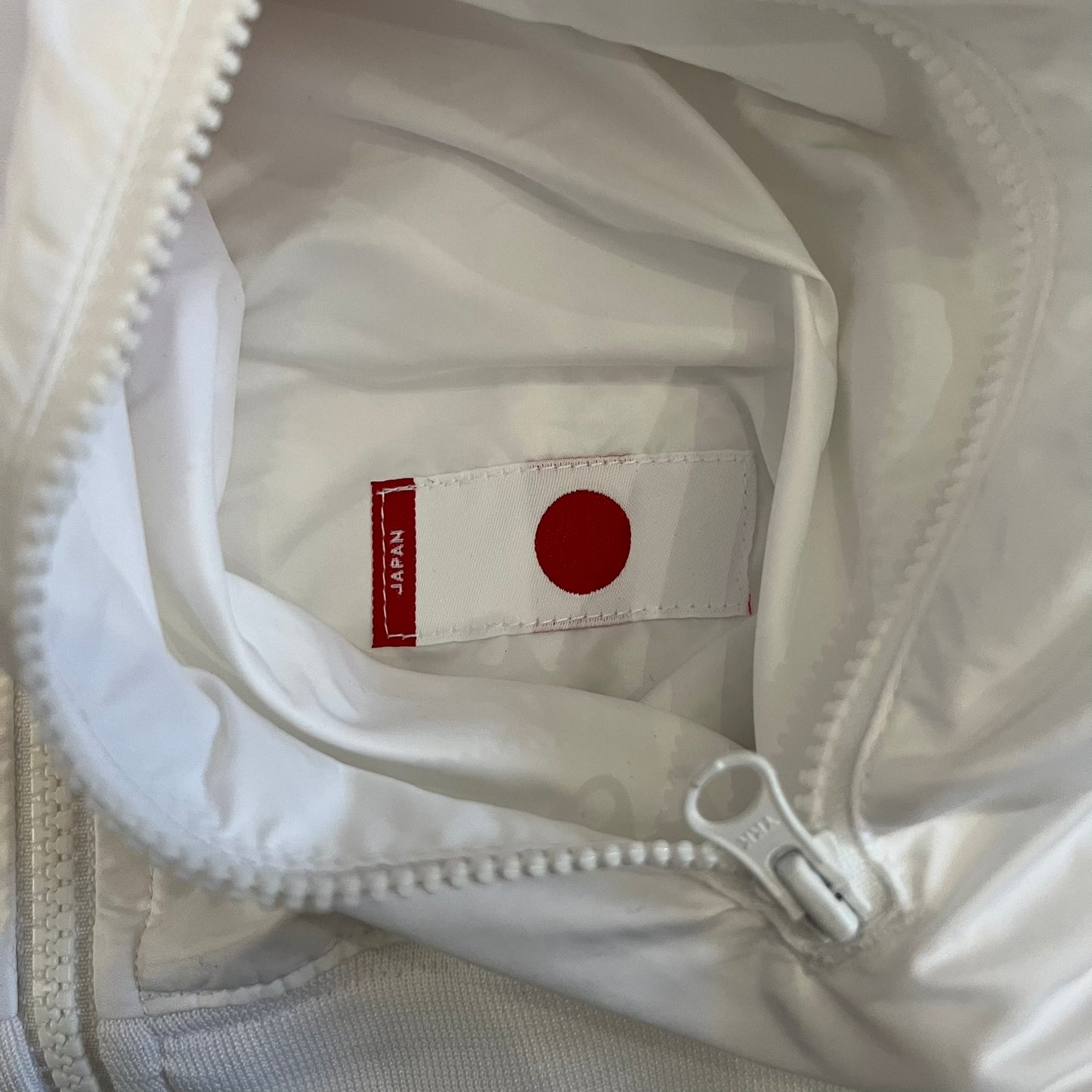 Nike Japan Olympics Split Windbreaker from 2008, created by designer Jarrett Reynolds. Crafted in white with a large red circle representing Japan’s flag, this innovative jacket can be zipped apart on both sides and merged with other compatible models. Hidden inside, a small Japan flags accent completes the concept.