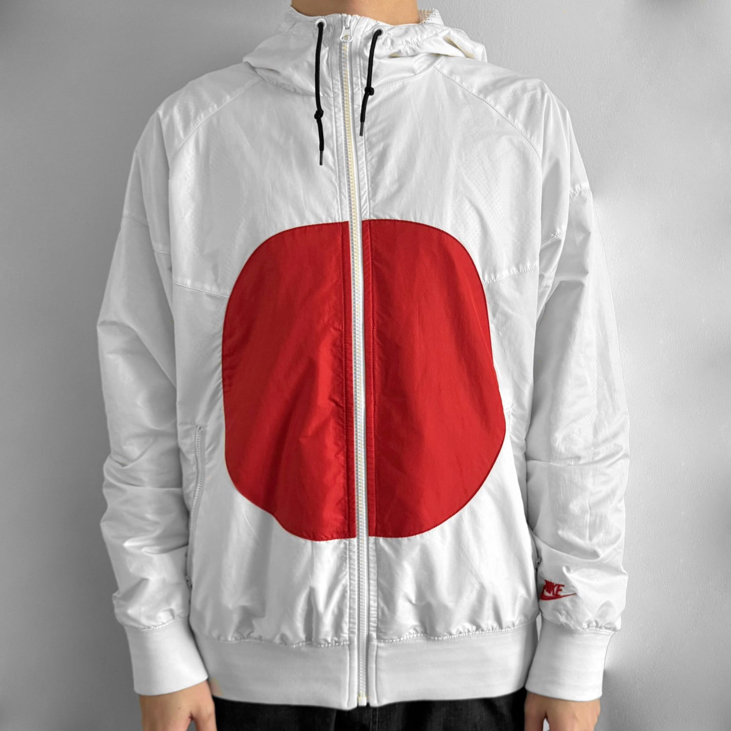 Nike Japan Olympics Split Windbreaker from 2008, created by designer Jarrett Reynolds. Crafted in white with a large red circle representing Japan’s flag, this innovative jacket can be zipped apart on both sides and merged with other compatible models. Hidden inside, a small Japan flags accent completes the concept.