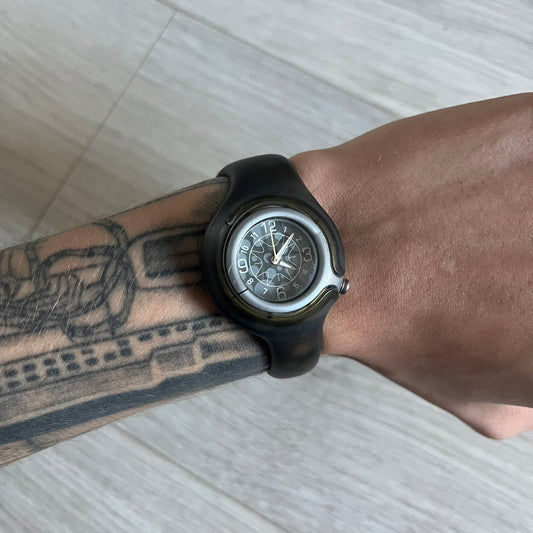 A minimalist timepiece from Nike, the Jelly Bean WK0003 stands out with its transparent dark strap filled with intentional bubble accents. The small analog face continues the theme with subtle grey bubble details, creating a sleek and unconventional design.