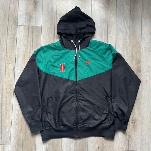 Nike Kenya Olympics Split Windbreaker from 2008, created by designer Jarrett Reynolds. Crafted in black and green. Small Maasai shield on one side of the chest with Nike red embroidery on the other. The upper half of the jacket is green, bottom and arms are fully black. This innovative jacket can be zipped apart on both sides and merged with other compatible models. Hidden inside, a small Kenya flags accent completes the concept.