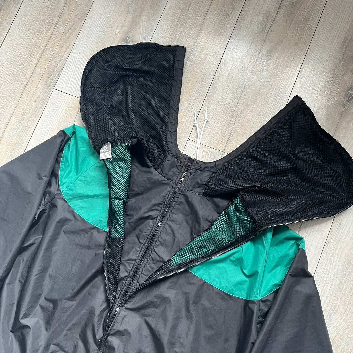 Nike Kenya Olympics Split Windbreaker from 2008, created by designer Jarrett Reynolds. Crafted in black and green. Small Maasai shield on one side of the chest with Nike red embroidery on the other. The upper half of the jacket is green, bottom and arms are fully black. This innovative jacket can be zipped apart on both sides and merged with other compatible models. Hidden inside, a small Kenya flags accent completes the concept.