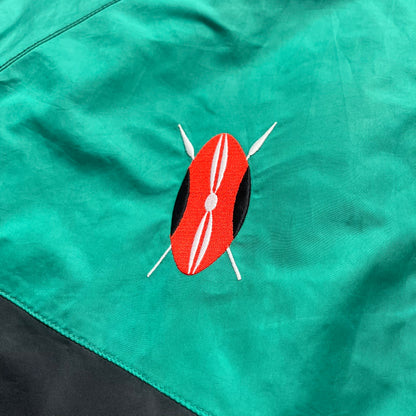 Nike Kenya Olympics Split Windbreaker from 2008, created by designer Jarrett Reynolds. Crafted in black and green. Small Maasai shield on one side of the chest with Nike red embroidery on the other. The upper half of the jacket is green, bottom and arms are fully black. This innovative jacket can be zipped apart on both sides and merged with other compatible models. Hidden inside, a small Kenya flags accent completes the concept.
