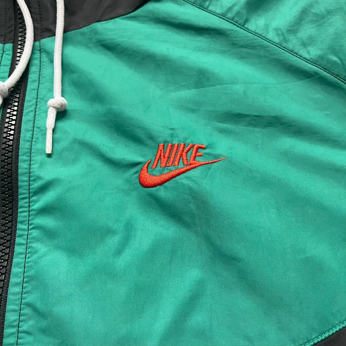 Nike Kenya Olympics Split Windbreaker from 2008, created by designer Jarrett Reynolds. Crafted in black and green. Small Maasai shield on one side of the chest with Nike red embroidery on the other. The upper half of the jacket is green, bottom and arms are fully black. This innovative jacket can be zipped apart on both sides and merged with other compatible models. Hidden inside, a small Kenya flags accent completes the concept.
