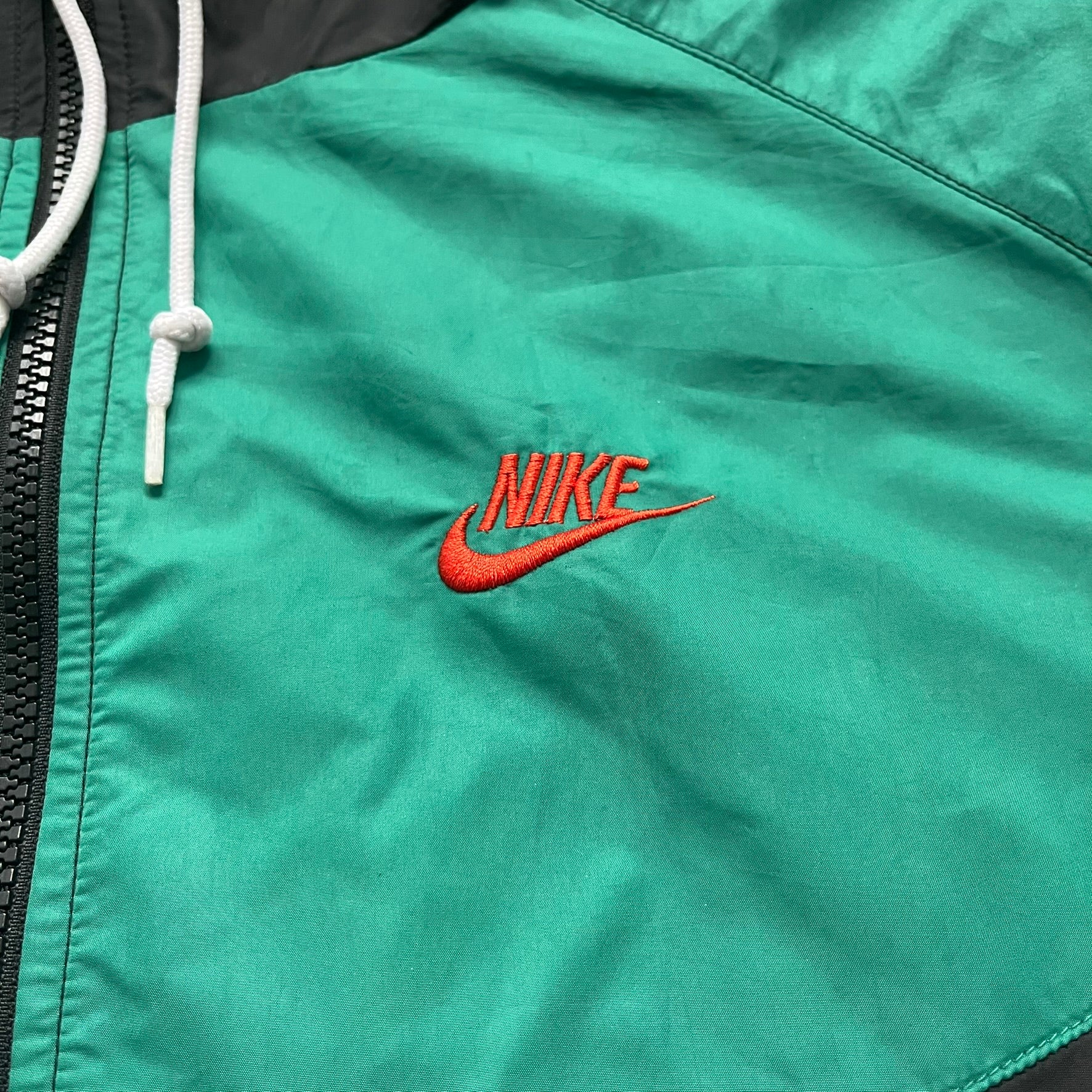 Nike Kenya Olympics Split Windbreaker from 2008, created by designer Jarrett Reynolds. Crafted in black and green. Small Maasai shield on one side of the chest with Nike red embroidery on the other. The upper half of the jacket is green, bottom and arms are fully black. This innovative jacket can be zipped apart on both sides and merged with other compatible models. Hidden inside, a small Kenya flags accent completes the concept.