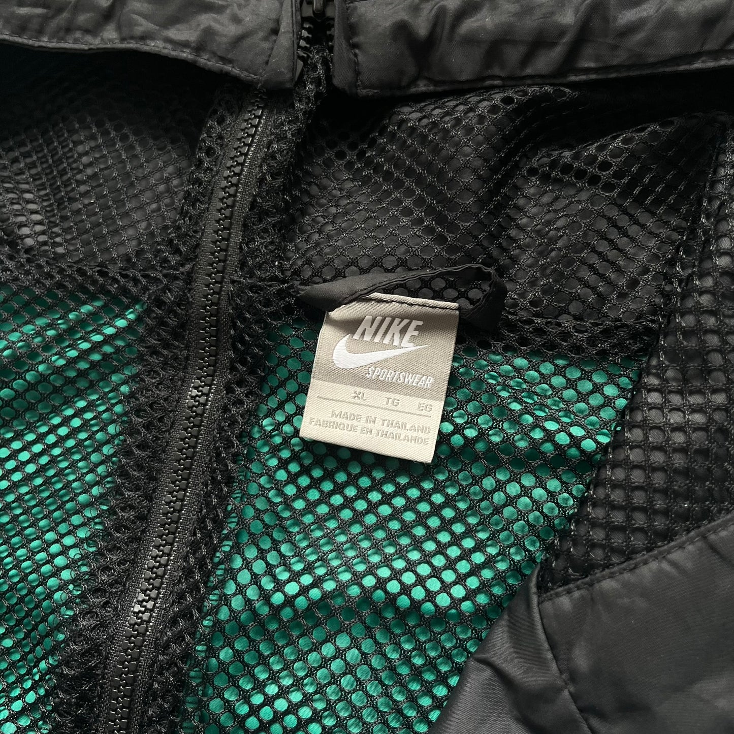 Nike Kenya Olympics Split Windbreaker from 2008, created by designer Jarrett Reynolds. Crafted in black and green. Small Maasai shield on one side of the chest with Nike red embroidery on the other. The upper half of the jacket is green, bottom and arms are fully black. This innovative jacket can be zipped apart on both sides and merged with other compatible models. Hidden inside, a small Kenya flags accent completes the concept.
