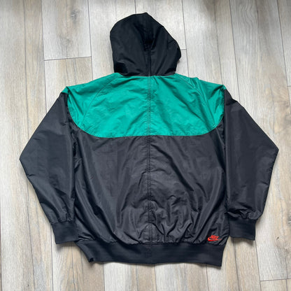 Nike Kenya Olympics Split Windbreaker from 2008, created by designer Jarrett Reynolds. Crafted in black and green. Small Maasai shield on one side of the chest with Nike red embroidery on the other. The upper half of the jacket is green, bottom and arms are fully black. This innovative jacket can be zipped apart on both sides and merged with other compatible models. Hidden inside, a small Kenya flags accent completes the concept.