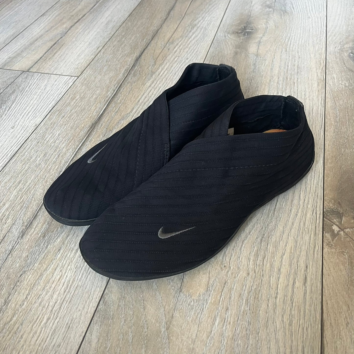 Nike Kyoto 2002 Slip-On Black Shoe is a slip-on model released in 2002, featuring a woven stretch upper with an embroidered Swoosh and stitched medial detailing. The design includes a nubuck panel with embossed Nike script and a patterned upper inspired by Zen garden textures, paired with a contrasting orange outsole. This model was part of Nike’s early performance-focused footwear line connected to yoga-inspired design.
