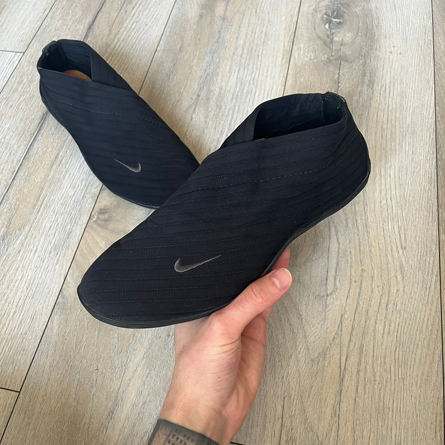 Nike Kyoto 2002 Slip-On Black Shoe is a slip-on model released in 2002, featuring a woven stretch upper with an embroidered Swoosh and stitched medial detailing. The design includes a nubuck panel with embossed Nike script and a patterned upper inspired by Zen garden textures, paired with a contrasting orange outsole. This model was part of Nike’s early performance-focused footwear line connected to yoga-inspired design.