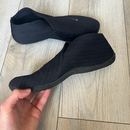 Nike Kyoto 2002 Slip-On Black Shoe is a slip-on model released in 2002, featuring a woven stretch upper with an embroidered Swoosh and stitched medial detailing. The design includes a nubuck panel with embossed Nike script and a patterned upper inspired by Zen garden textures, paired with a contrasting orange outsole. This model was part of Nike’s early performance-focused footwear line connected to yoga-inspired design.