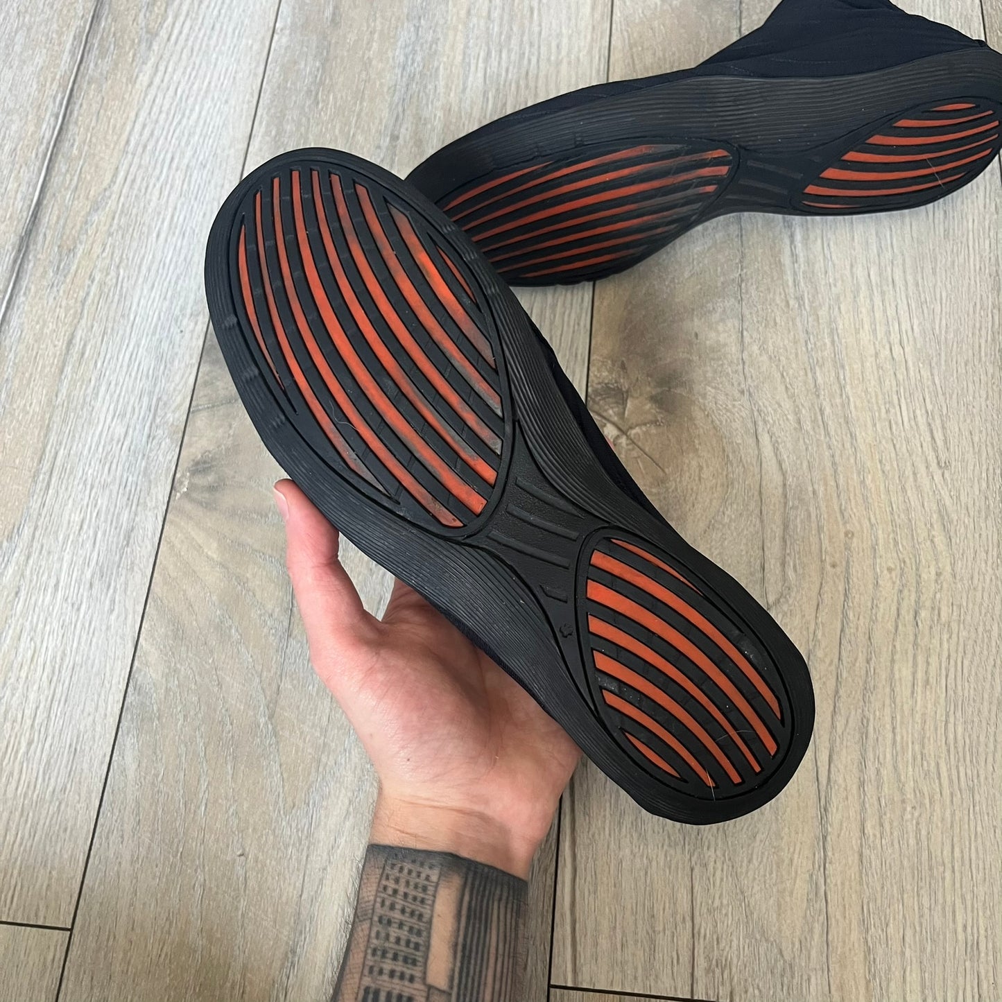 Nike Kyoto 2002 Slip-On Black Shoe is a slip-on model released in 2002, featuring a woven stretch upper with an embroidered Swoosh and stitched medial detailing. The design includes a nubuck panel with embossed Nike script and a patterned upper inspired by Zen garden textures, paired with a contrasting orange outsole. This model was part of Nike’s early performance-focused footwear line connected to yoga-inspired design.