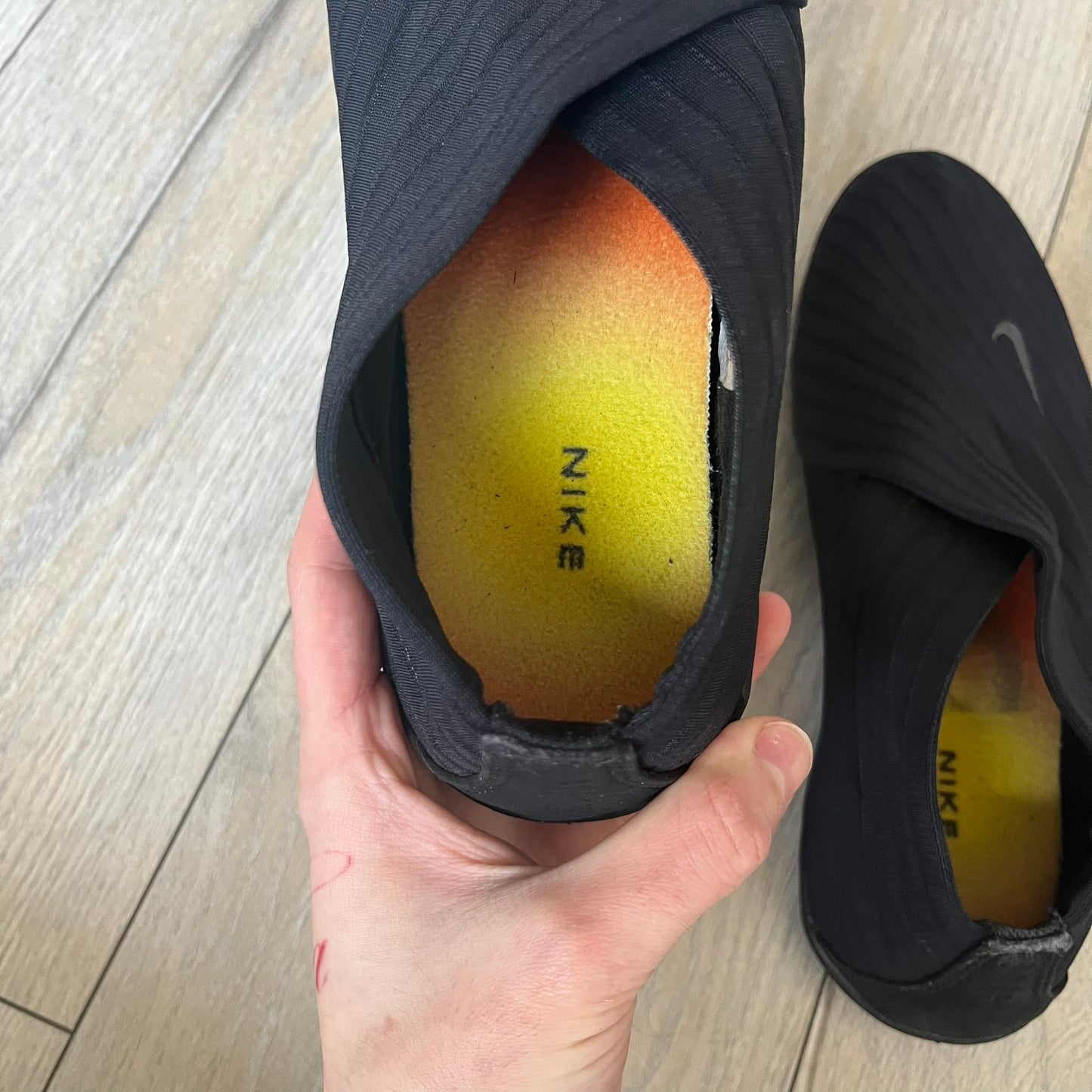 Nike Kyoto 2002 Slip-On Black Shoe is a slip-on model released in 2002, featuring a woven stretch upper with an embroidered Swoosh and stitched medial detailing. The design includes a nubuck panel with embossed Nike script and a patterned upper inspired by Zen garden textures, paired with a contrasting orange outsole. This model was part of Nike’s early performance-focused footwear line connected to yoga-inspired design.
