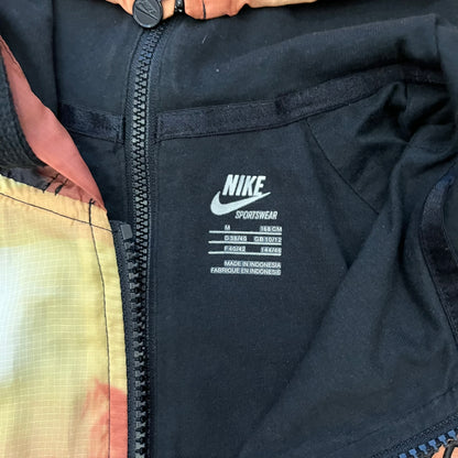Nike “Beach Sunset” Split Windbreaker WMNS features dual zippers along the front and back, allowing the jacket to separate and merge with other compatible models from the collection. The all-over print shows an orange and yellow sunset with black palms, complemented by black hems and interior lining. Finished with circular metal Nike zip pulls and a small black embroidered Swoosh on the right chest.