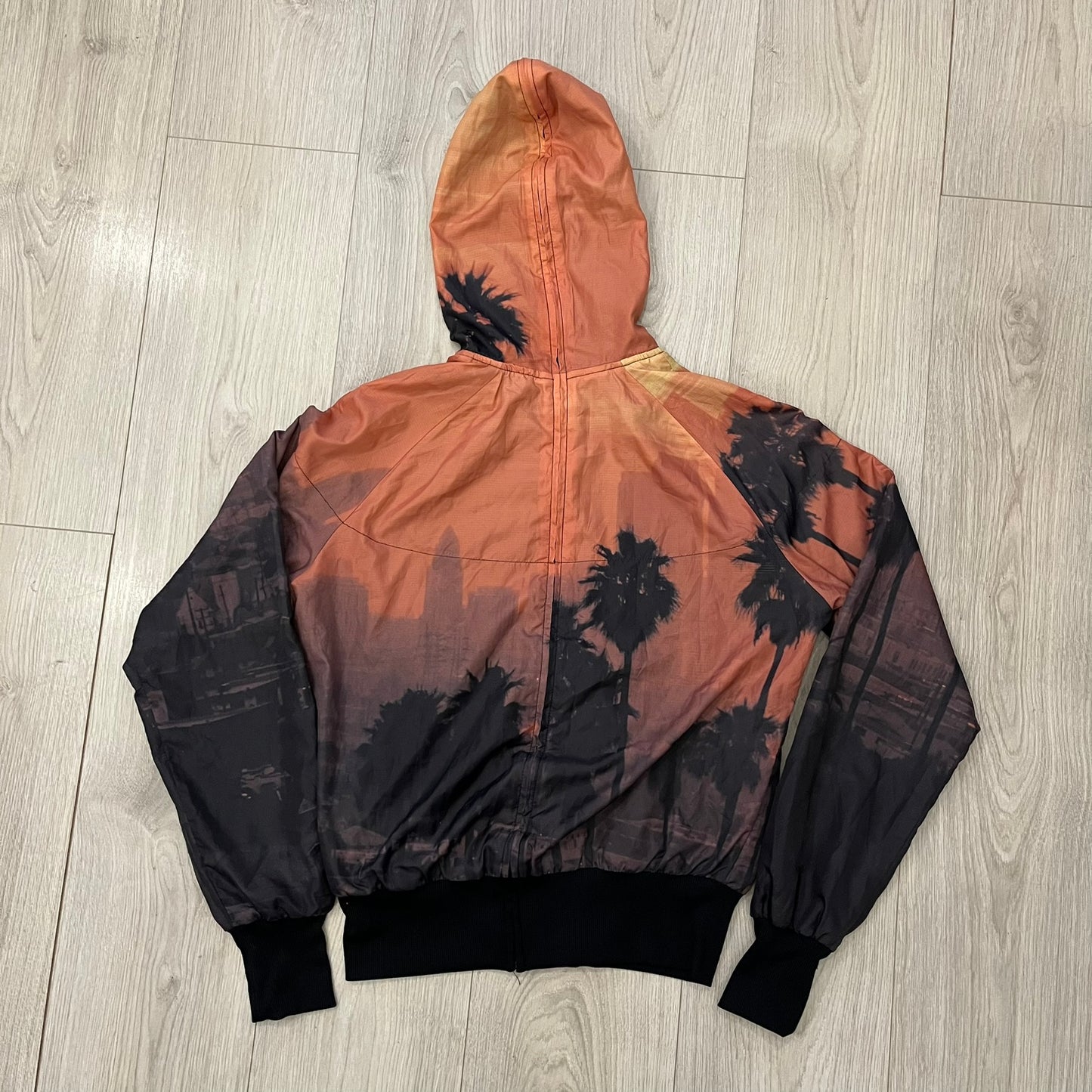 Nike “Beach Sunset” Split Windbreaker WMNS features dual zippers along the front and back, allowing the jacket to separate and merge with other compatible models from the collection. The all-over print shows an orange and yellow sunset with black palms, complemented by black hems and interior lining. Finished with circular metal Nike zip pulls and a small black embroidered Swoosh on the right chest.