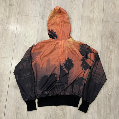 Nike “Beach Sunset” Split Windbreaker WMNS features dual zippers along the front and back, allowing the jacket to separate and merge with other compatible models from the collection. The all-over print shows an orange and yellow sunset with black palms, complemented by black hems and interior lining. Finished with circular metal Nike zip pulls and a small black embroidered Swoosh on the right chest.