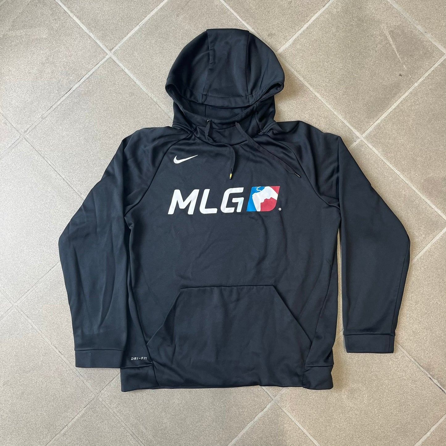 Nike MLG (Major League Gaming) Black Hoodie is a performance hoodie made from 100% polyester with Nike Dri-FIT technology. It features a kangaroo pocket, a Nike Swoosh on the upper right chest, and a large Major League Gaming (MLG) logo across the center with the iconic red and blue gamepad graphic. The hood has a raised front design that extends to cover the mouth.