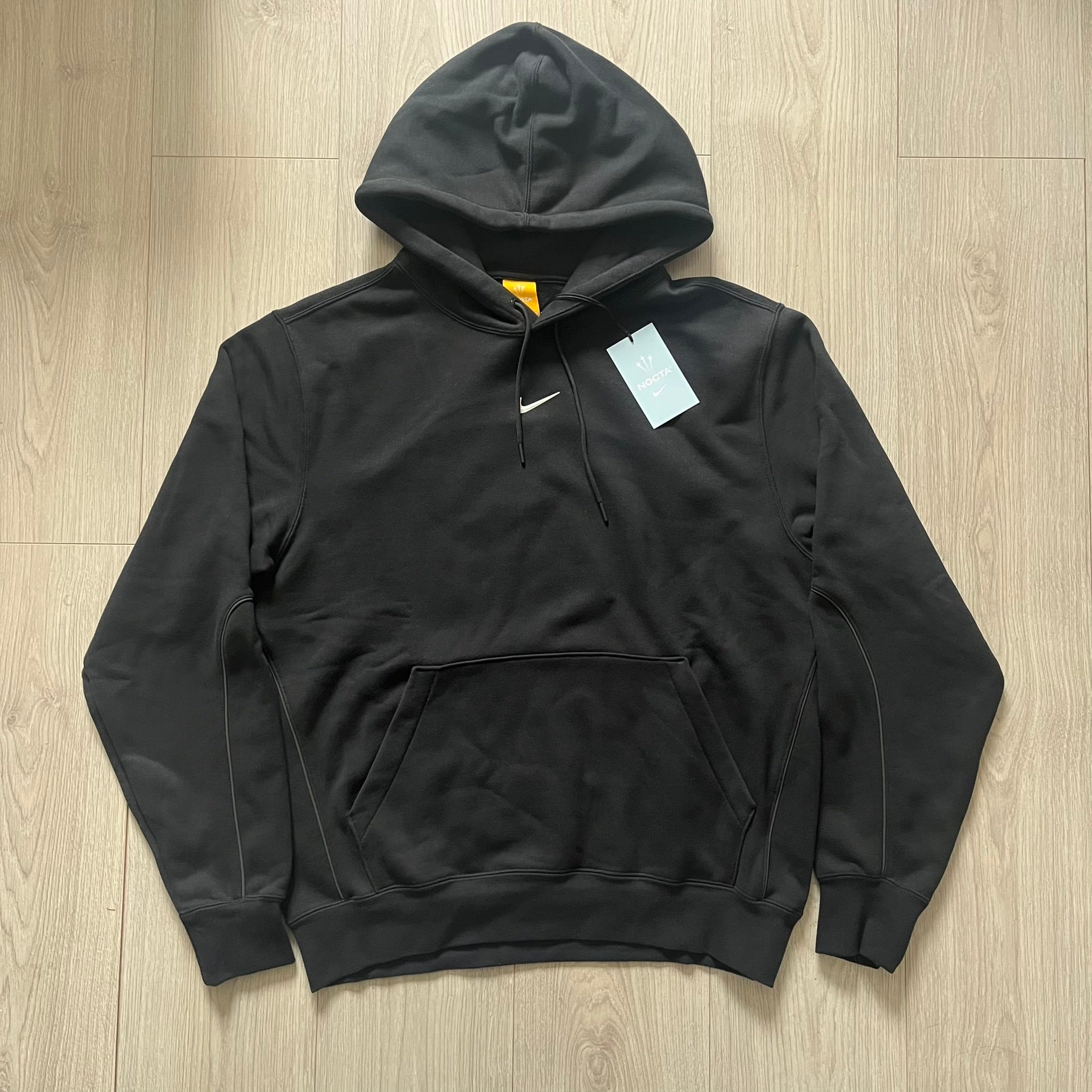 Nike x Nocta Fleece CS Hoodie in Black combines Drake’s refined streetwear vision with Nike’s premium craftsmanship. Made from an ultra-soft fleece blend, it features reflective piping, a silicone Swoosh logo and discreet NOCTA branding. With an adjustable hood, kangaroo pocket, and hidden zip pocket, this piece balances luxury comfort and technical precision.