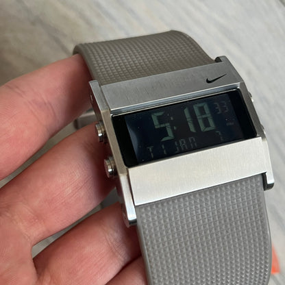 Nike Oregon Series Square Black Face Digital Watch WA0036-201 is a digital wristwatch featuring a rectangular display with a stainless steel frame and a light grey rubber strap with stainless steel clasp. The watch includes four side buttons, backlight function, and displays digital numerals on a black screen, with a small Nike logo on the metal bezel. It is water resistant up to 100 meters, powered by fresh batteries, and comes with original tag and box