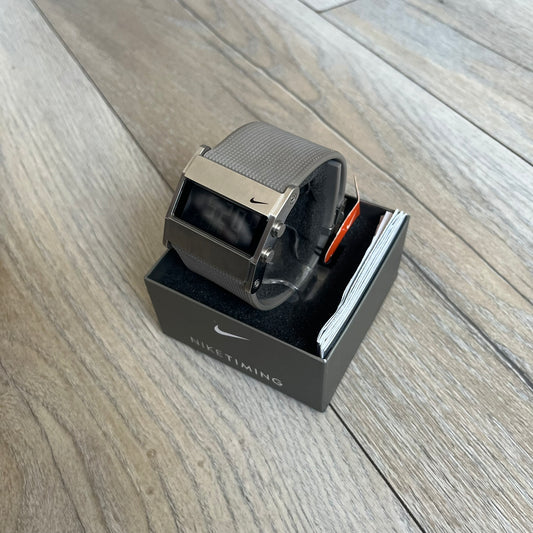 Nike Oregon Series Square Black Face Digital Watch WA0036-201 is a digital wristwatch featuring a rectangular display with a stainless steel frame and a light grey rubber strap with stainless steel clasp. The watch includes four side buttons, backlight function, and displays digital numerals on a black screen, with a small Nike logo on the metal bezel. It is water resistant up to 100 meters, powered by fresh batteries, and comes with original tag and box