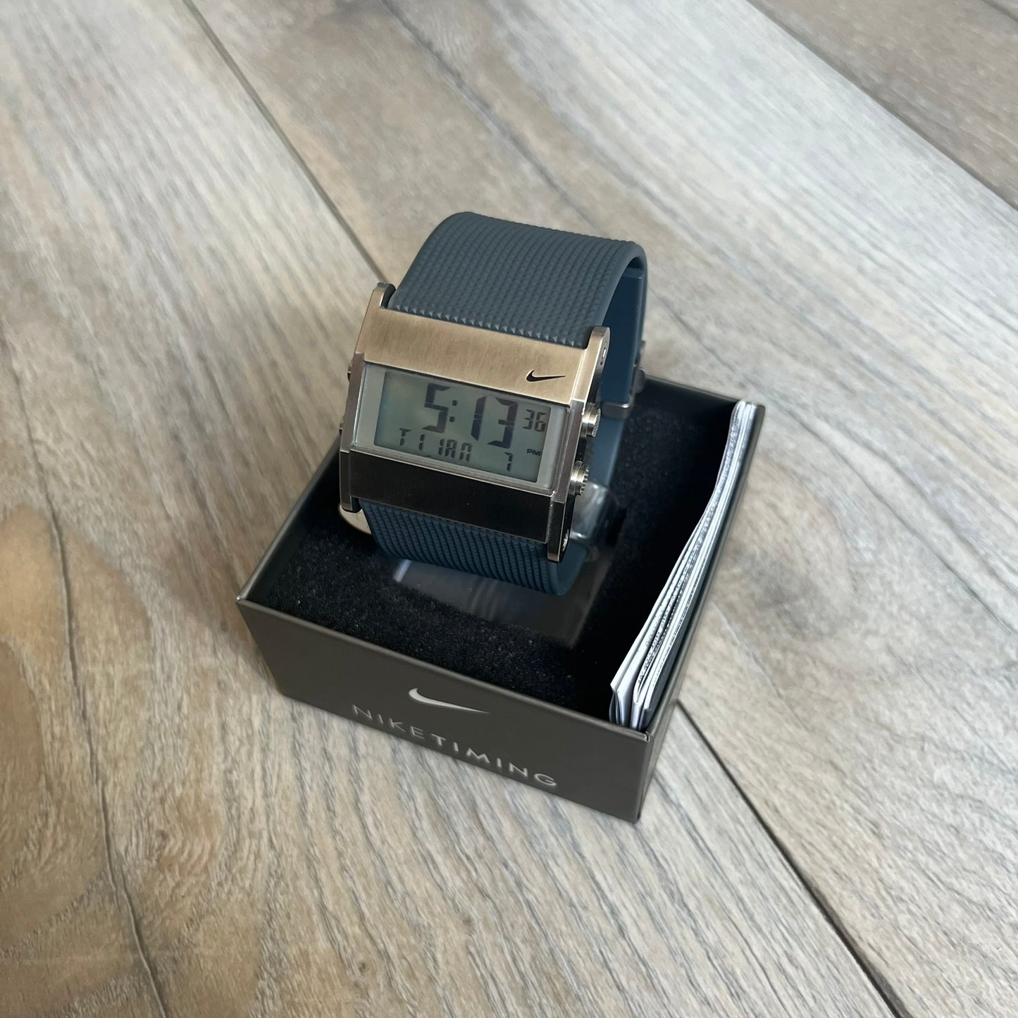 Nike Oregon Series Gray Digital Watch is a digital wristwatch featuring a rectangular display with a stainless steel frame and a dark grey rubber strap with stainless steel clasp. The watch includes four side buttons, backlight function, and displays black digital numerals, with a small Nike logo on the metal bezel. It is water resistant up to 100 meters, powered by fresh batteries, and comes with original tag and box.