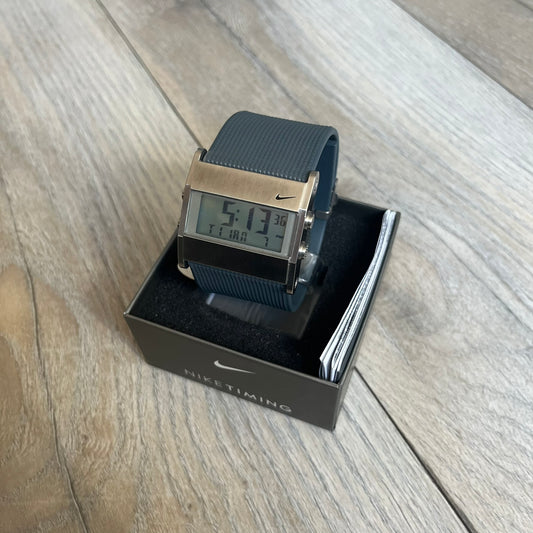 Nike Oregon Series Gray Digital Watch is a digital wristwatch featuring a rectangular display with a stainless steel frame and a dark grey rubber strap with stainless steel clasp. The watch includes four side buttons, backlight function, and displays black digital numerals, with a small Nike logo on the metal bezel. It is water resistant up to 100 meters, powered by fresh batteries, and comes with original tag and box.