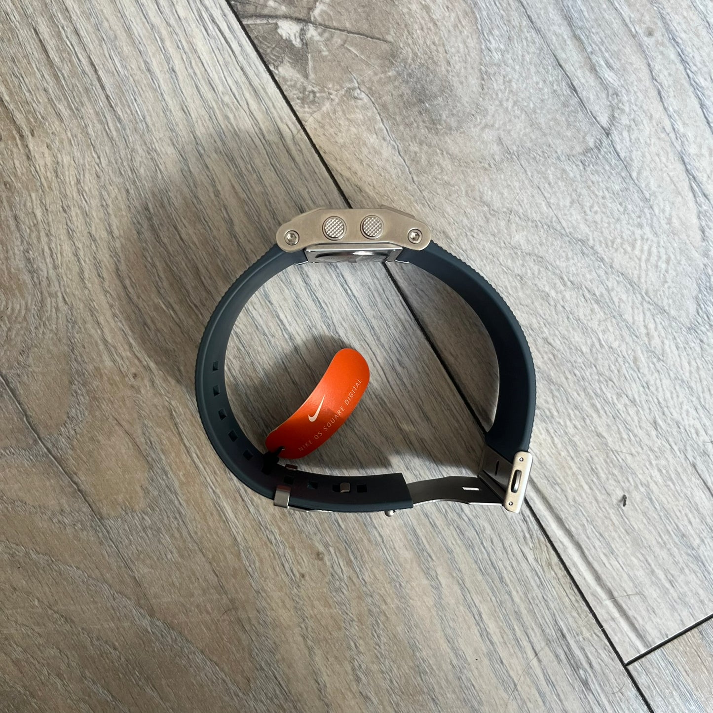 Nike Oregon Series Gray Digital Watch is a digital wristwatch featuring a rectangular display with a stainless steel frame and a dark grey rubber strap with stainless steel clasp. The watch includes four side buttons, backlight function, and displays black digital numerals, with a small Nike logo on the metal bezel. It is water resistant up to 100 meters, powered by fresh batteries, and comes with original tag and box.