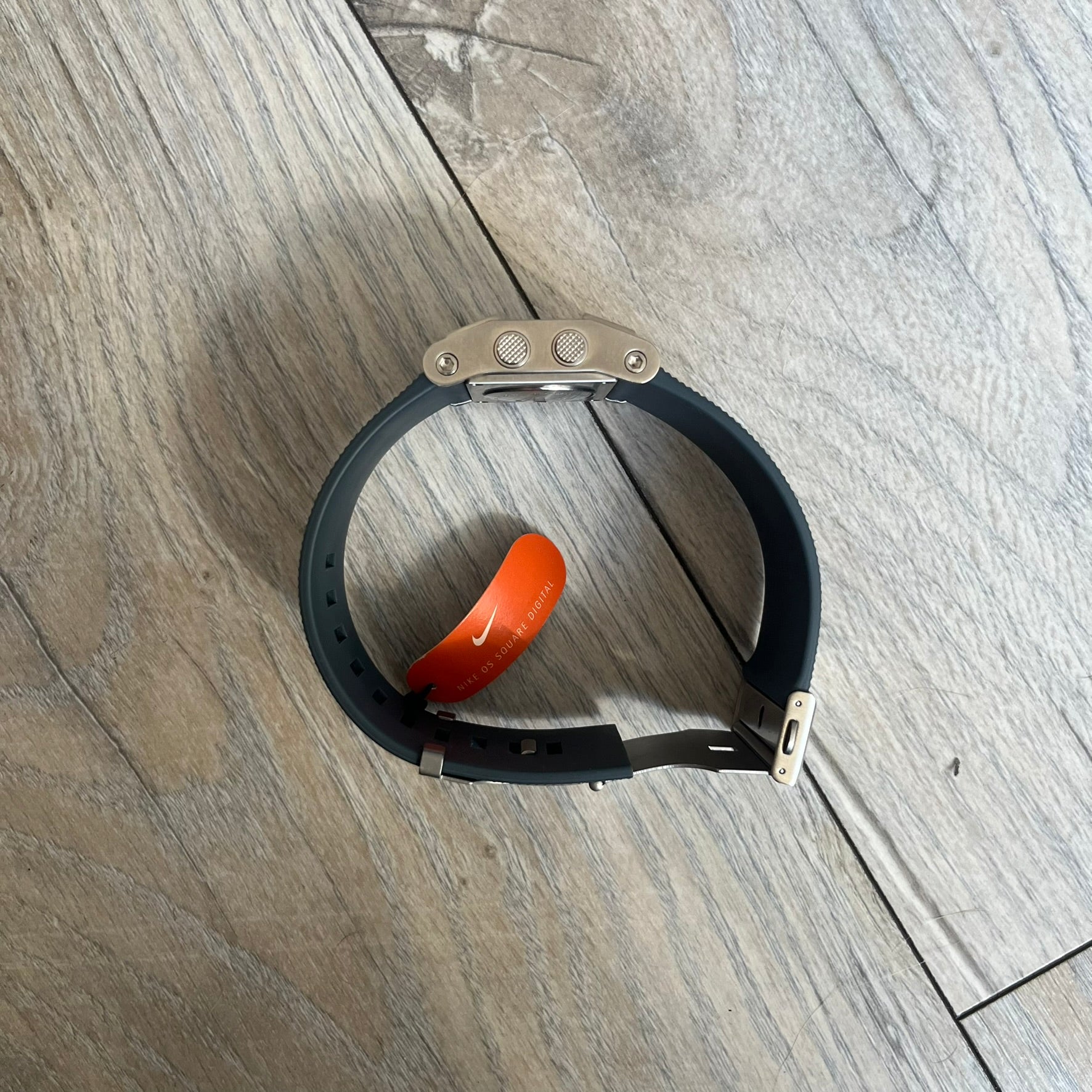 Nike Oregon Series Gray Digital Watch is a digital wristwatch featuring a rectangular display with a stainless steel frame and a dark grey rubber strap with stainless steel clasp. The watch includes four side buttons, backlight function, and displays black digital numerals, with a small Nike logo on the metal bezel. It is water resistant up to 100 meters, powered by fresh batteries, and comes with original tag and box.