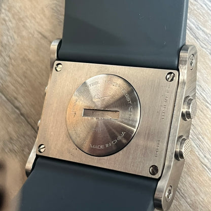 Nike Oregon Series Gray Digital Watch is a digital wristwatch featuring a rectangular display with a stainless steel frame and a dark grey rubber strap with stainless steel clasp. The watch includes four side buttons, backlight function, and displays black digital numerals, with a small Nike logo on the metal bezel. It is water resistant up to 100 meters, powered by fresh batteries, and comes with original tag and box.