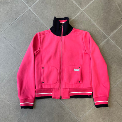 Nike Pink Women's Bomber-style Zip-up features a pink, heavyweight cotton construction with a tall black collar. It has a full front zipper with a circular zipper pull and two front Velcro pockets, one with a small Nike tag. The garment has a jacket-style construction.
