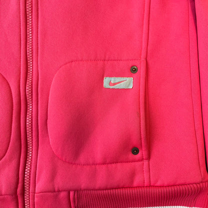 Nike Pink Women's Bomber-style Zip-up features a pink, heavyweight cotton construction with a tall black collar. It has a full front zipper with a circular zipper pull and two front Velcro pockets, one with a small Nike tag. The garment has a jacket-style construction.
