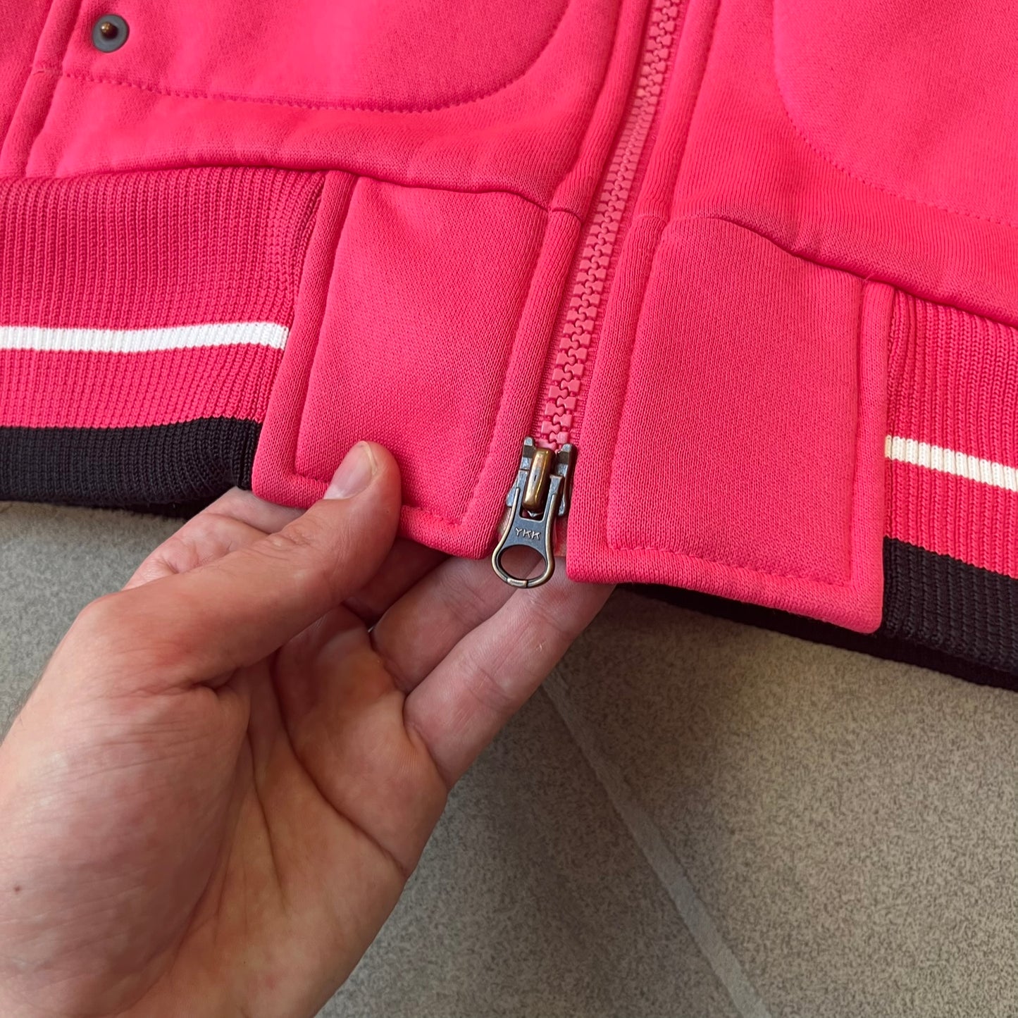 Nike Pink Women's Bomber-style Zip-up features a pink, heavyweight cotton construction with a tall black collar. It has a full front zipper with a circular zipper pull and two front Velcro pockets, one with a small Nike tag. The garment has a jacket-style construction.
