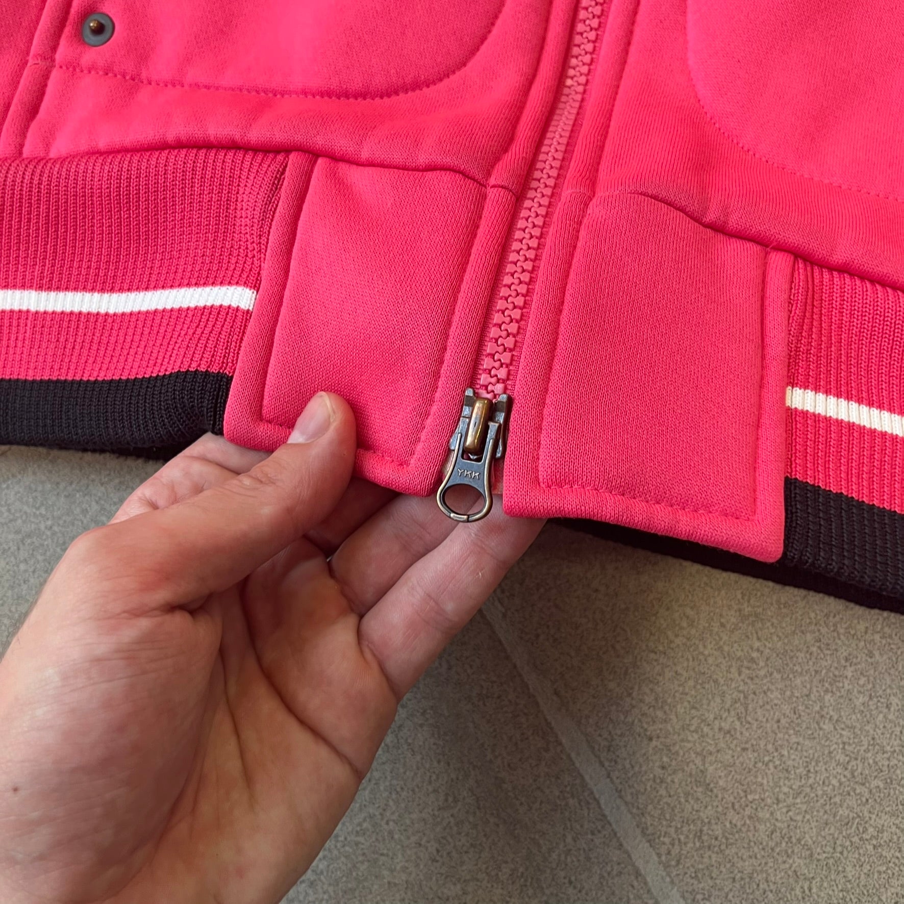 Nike Pink Women's Bomber-style Zip-up features a pink, heavyweight cotton construction with a tall black collar. It has a full front zipper with a circular zipper pull and two front Velcro pockets, one with a small Nike tag. The garment has a jacket-style construction.
