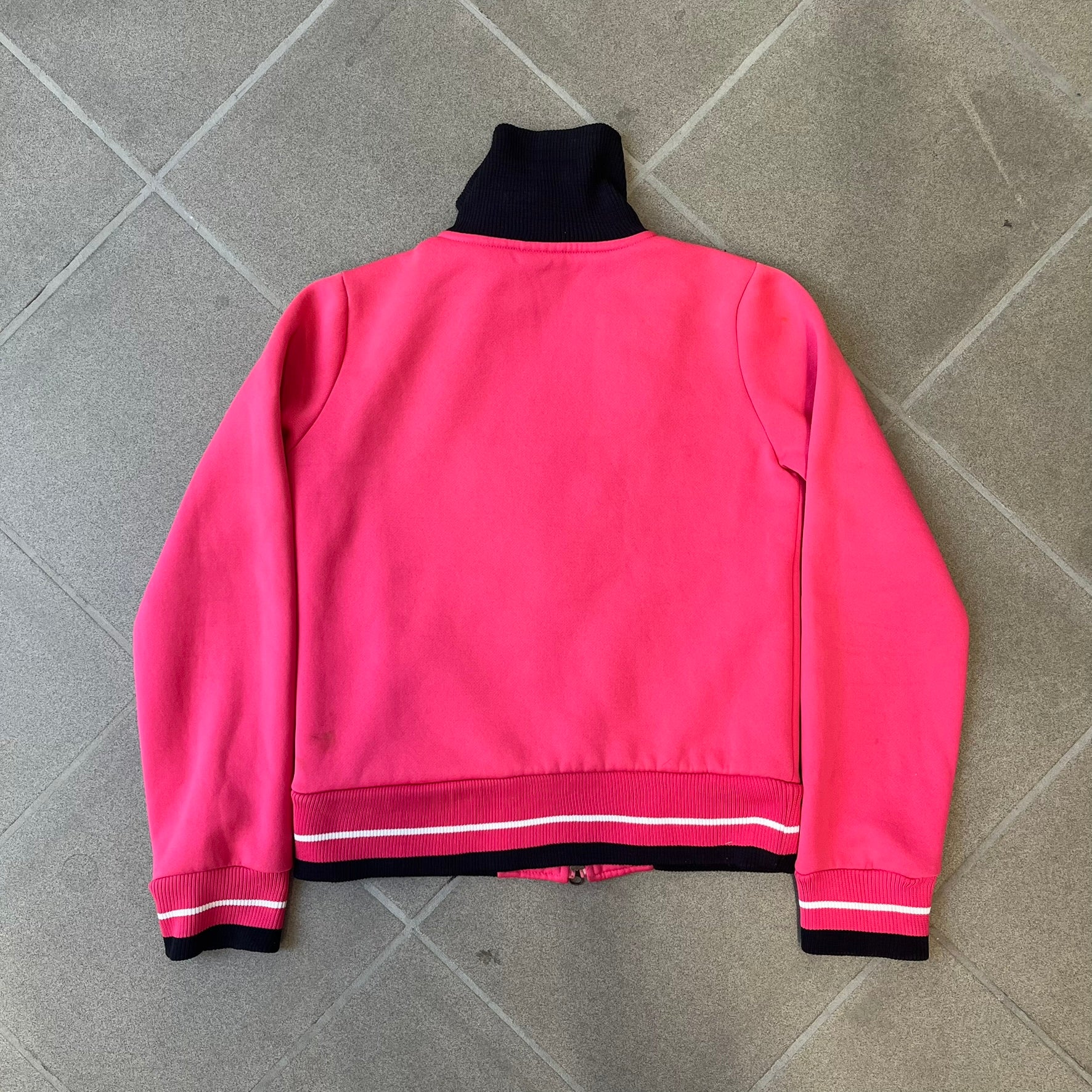 Nike Pink Women's Bomber-style Zip-up features a pink, heavyweight cotton construction with a tall black collar. It has a full front zipper with a circular zipper pull and two front Velcro pockets, one with a small Nike tag. The garment has a jacket-style construction.
